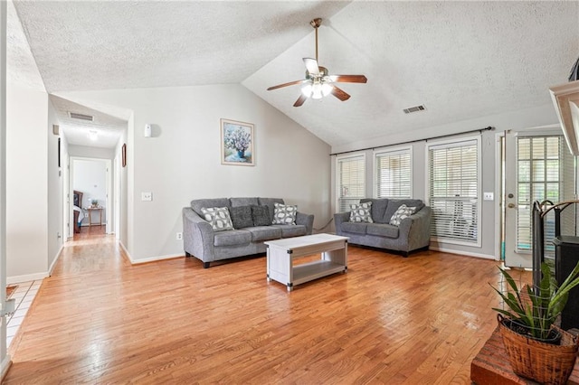 living area with light wood finished floors, ceiling fan, a textured ceiling, vaulted ceiling, and baseboards