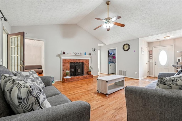 living room with a ceiling fan, light wood finished floors, vaulted ceiling, a textured ceiling, and a fireplace
