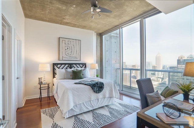 bedroom featuring a view of city, access to outside, wood finished floors, a wall of windows, and baseboards