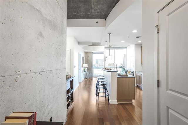 kitchen with visible vents, recessed lighting, a kitchen breakfast bar, dark wood-style floors, and a kitchen island with sink