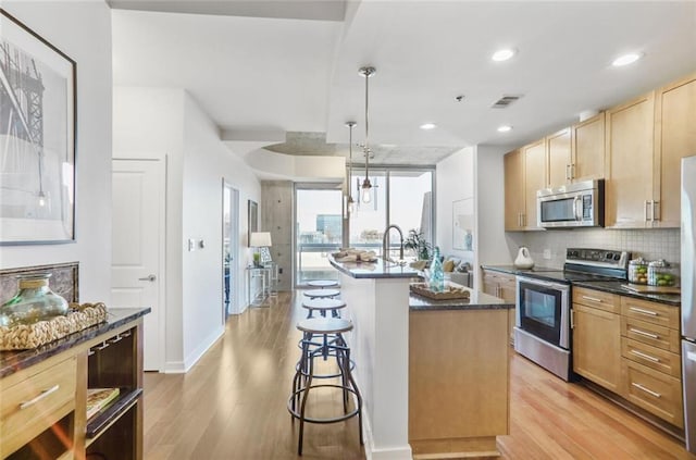 kitchen featuring visible vents, light wood-style floors, appliances with stainless steel finishes, and a breakfast bar area