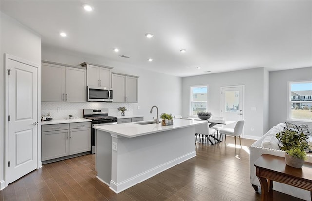 kitchen with backsplash, gray cabinets, a center island with sink, sink, and appliances with stainless steel finishes