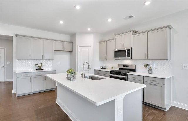 kitchen featuring stainless steel appliances, gray cabinetry, an island with sink, and sink