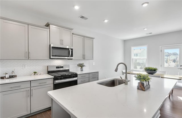 kitchen featuring sink, dark wood-type flooring, an island with sink, gray cabinetry, and stainless steel appliances