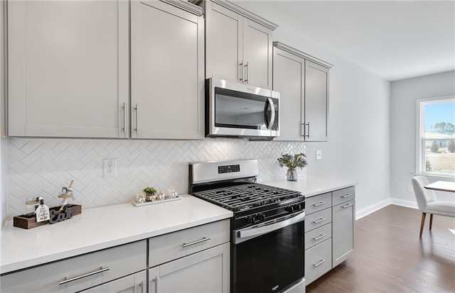 kitchen with decorative backsplash, appliances with stainless steel finishes, gray cabinets, and dark hardwood / wood-style flooring