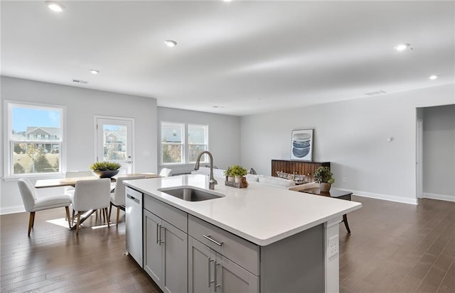 kitchen with a center island with sink, gray cabinetry, dark wood-type flooring, stainless steel dishwasher, and sink