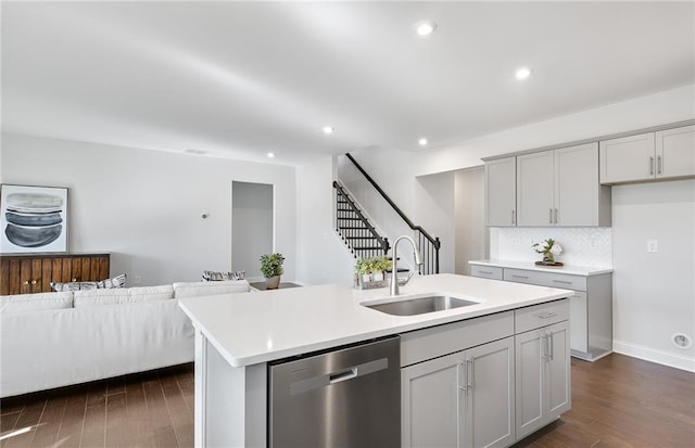 kitchen featuring gray cabinets, an island with sink, dark hardwood / wood-style flooring, stainless steel dishwasher, and sink