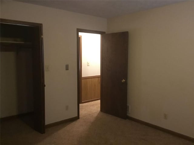 unfurnished bedroom with light carpet, a closet, and wooden walls