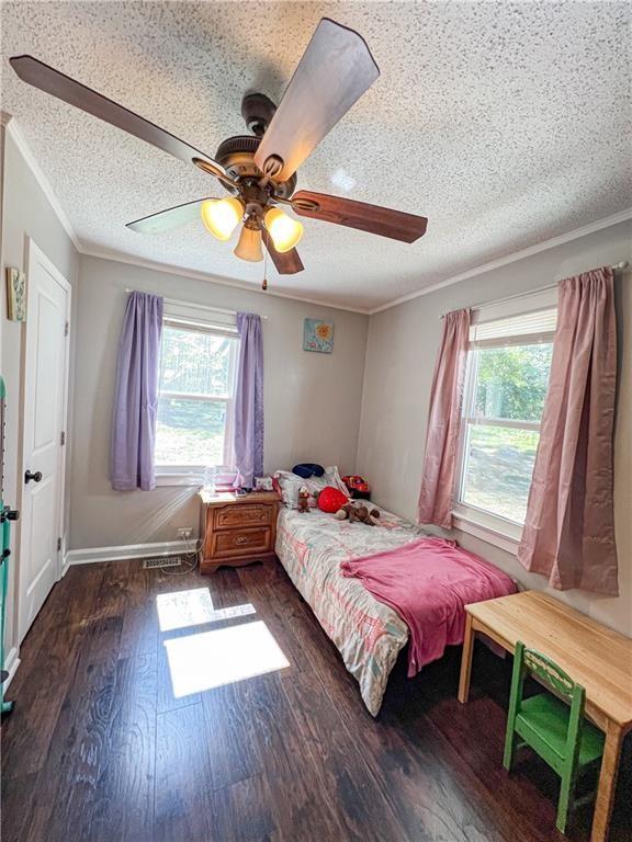 unfurnished bedroom with multiple windows, ornamental molding, and dark wood-type flooring