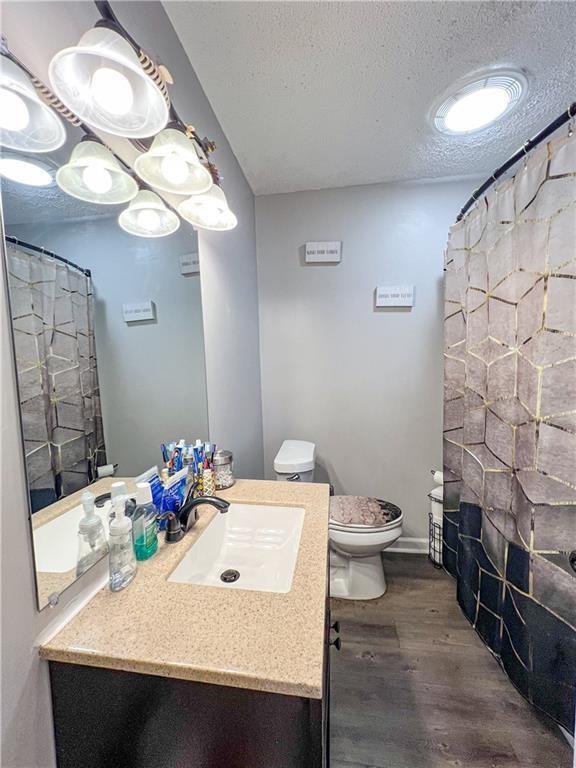 bathroom with toilet, wood-type flooring, a textured ceiling, vanity, and curtained shower