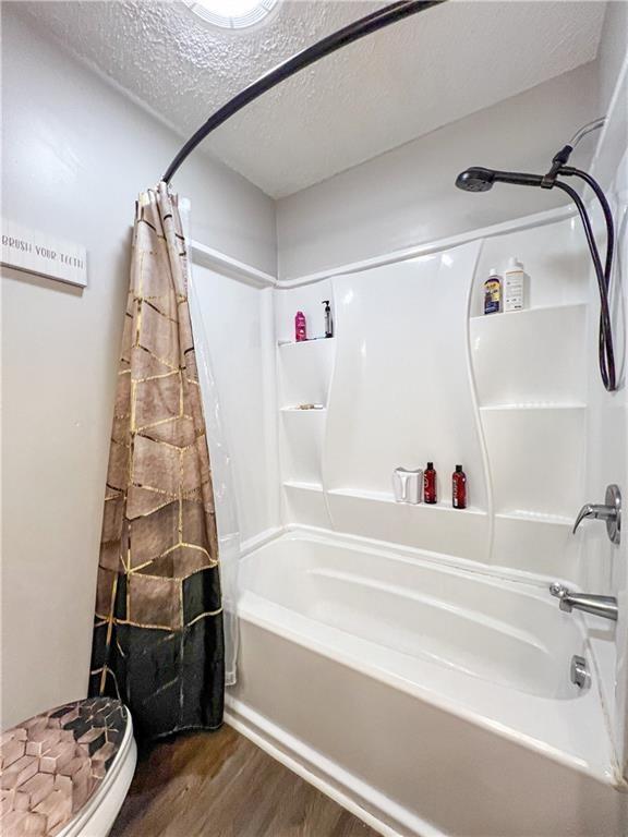 bathroom featuring hardwood / wood-style floors, shower / bathtub combination with curtain, a textured ceiling, and toilet