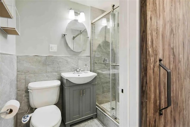 bathroom featuring a shower with door, vanity, tile walls, and toilet