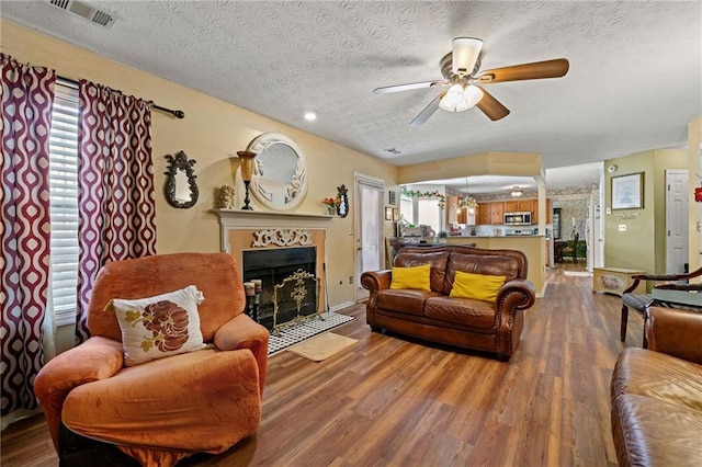 living area with visible vents, a textured ceiling, a tiled fireplace, and wood finished floors