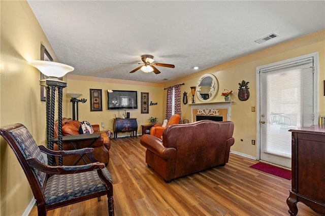 living area featuring baseboards, visible vents, ceiling fan, wood finished floors, and a fireplace