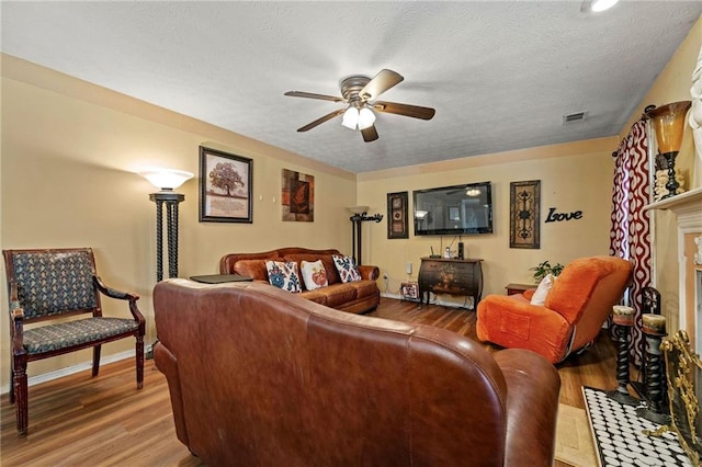 living area featuring visible vents, ceiling fan, wood finished floors, a textured ceiling, and a fireplace