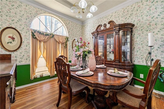 dining space featuring a wainscoted wall, crown molding, a notable chandelier, wood finished floors, and wallpapered walls