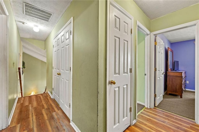 hall featuring visible vents, a textured ceiling, baseboards, and wood finished floors