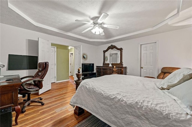 bedroom with a textured ceiling, light wood-style flooring, a ceiling fan, baseboards, and a raised ceiling