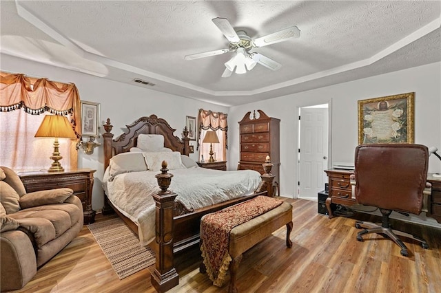 bedroom with a raised ceiling, visible vents, a textured ceiling, and light wood finished floors