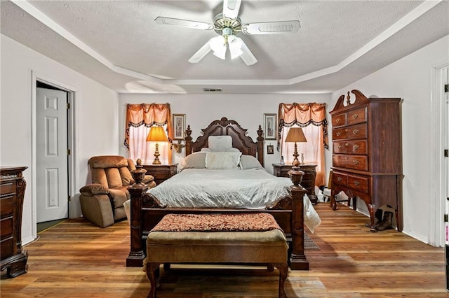 bedroom featuring a textured ceiling, wood finished floors, and a raised ceiling