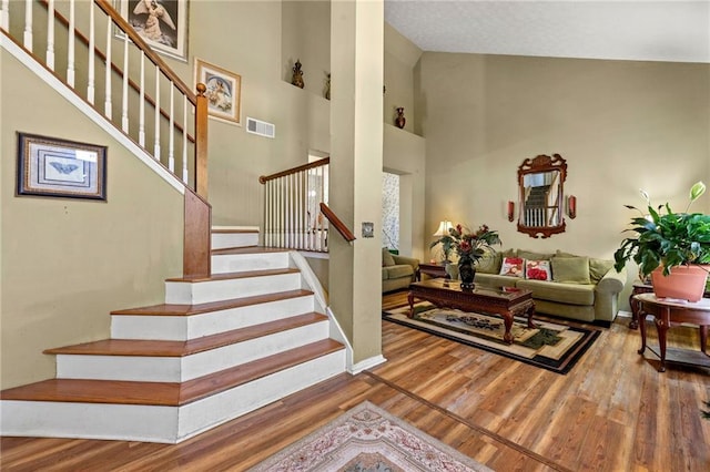 staircase featuring a high ceiling, wood finished floors, and visible vents