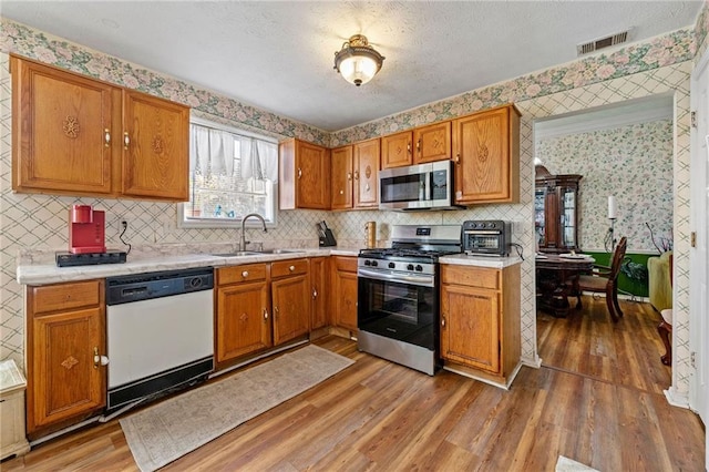 kitchen featuring light countertops, visible vents, appliances with stainless steel finishes, a sink, and wallpapered walls