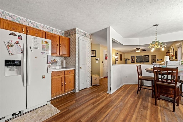 kitchen with white refrigerator with ice dispenser, dark wood-type flooring, light countertops, hanging light fixtures, and brown cabinetry