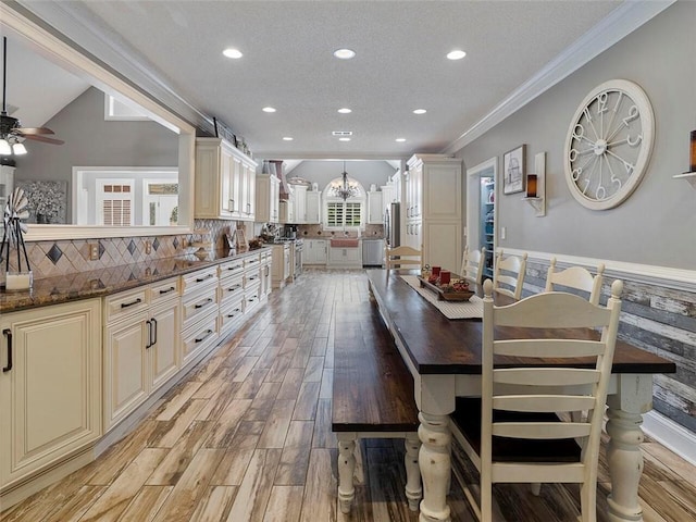 kitchen with ornamental molding, dark stone countertops, backsplash, decorative light fixtures, and ceiling fan with notable chandelier