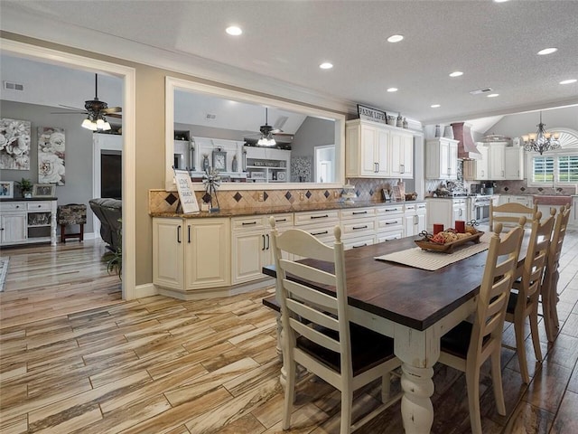 dining area featuring vaulted ceiling, a textured ceiling, ceiling fan with notable chandelier, sink, and light hardwood / wood-style flooring