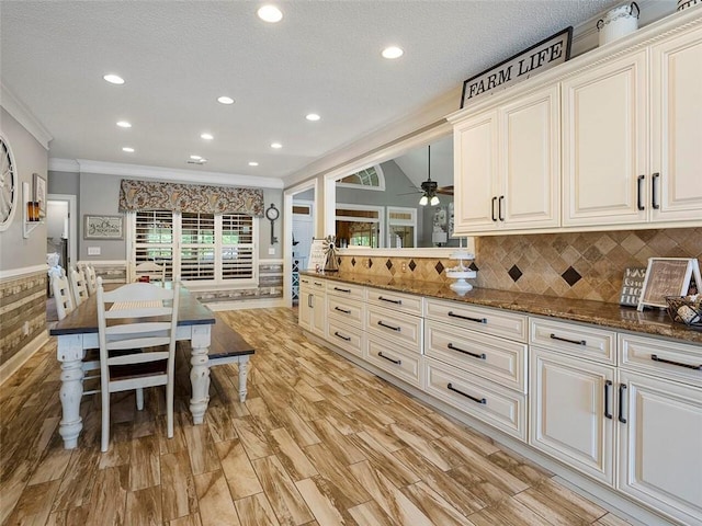 kitchen featuring backsplash, light hardwood / wood-style floors, dark stone countertops, ceiling fan, and ornamental molding