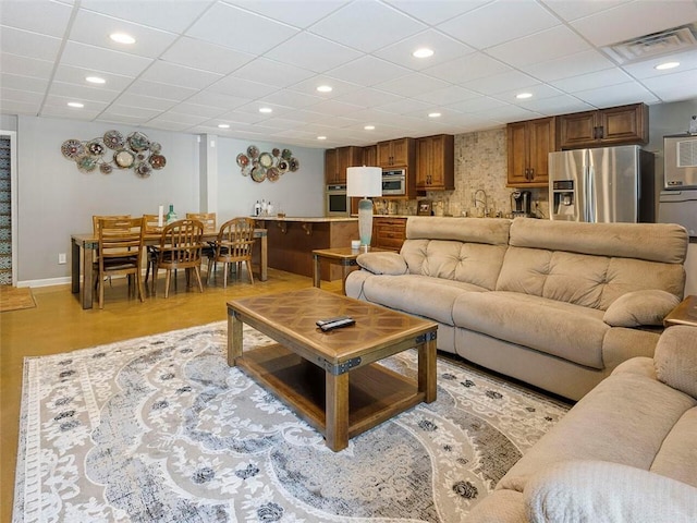 living room featuring a drop ceiling, sink, and light wood-type flooring