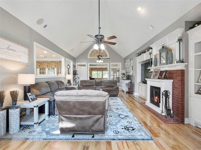 living room featuring ceiling fan, a brick fireplace, built in shelves, and light hardwood / wood-style floors