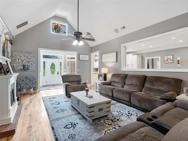 living room with a fireplace, high vaulted ceiling, ceiling fan, and light wood-type flooring