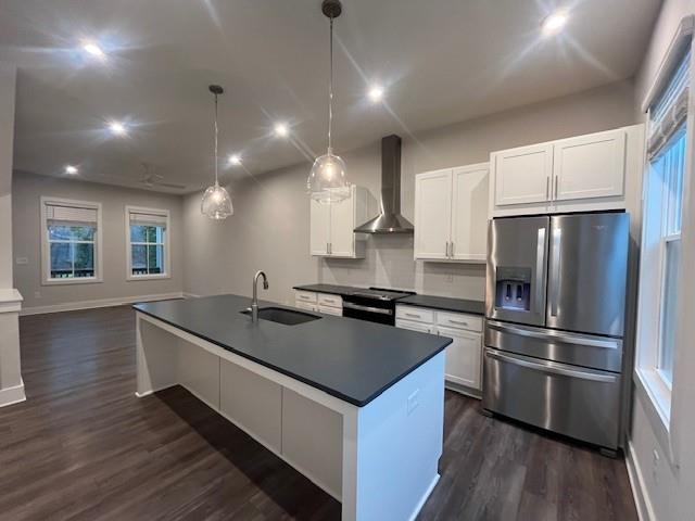 kitchen featuring stainless steel refrigerator with ice dispenser, wall chimney exhaust hood, sink, decorative light fixtures, and white cabinets