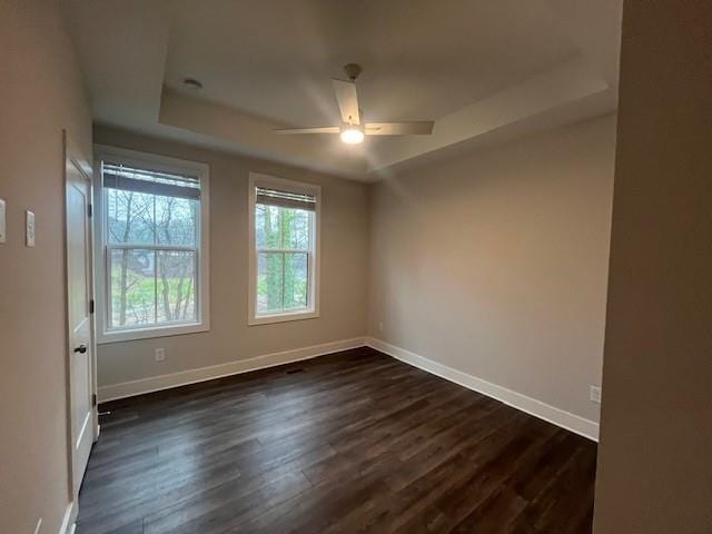 empty room featuring ceiling fan, a tray ceiling, and dark hardwood / wood-style flooring