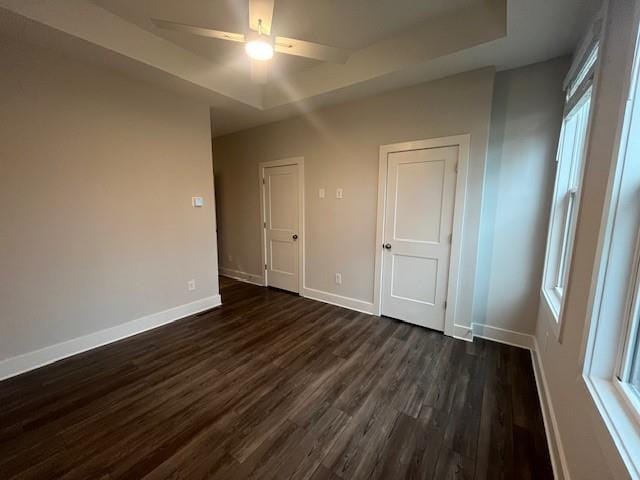 empty room featuring ceiling fan, a healthy amount of sunlight, dark hardwood / wood-style flooring, and a tray ceiling