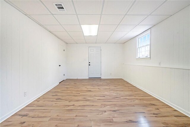 empty room featuring a paneled ceiling, wooden walls, and light hardwood / wood-style flooring