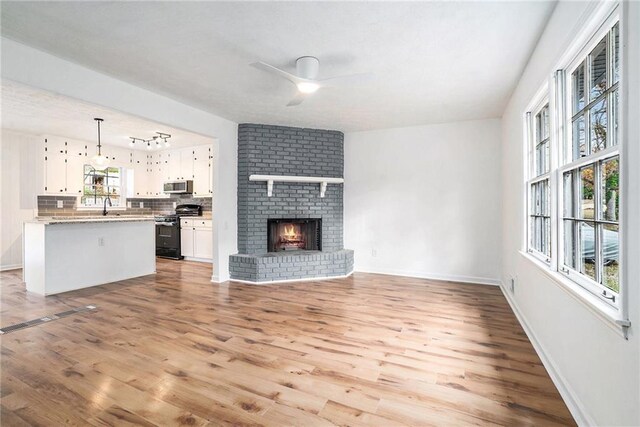 unfurnished living room with a brick fireplace, light hardwood / wood-style flooring, plenty of natural light, and ceiling fan