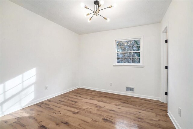 spare room with wood-type flooring and an inviting chandelier