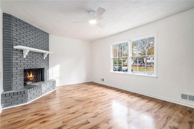 unfurnished living room with a brick fireplace, ceiling fan, a textured ceiling, and light hardwood / wood-style flooring