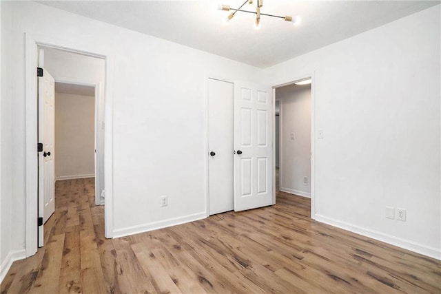 unfurnished bedroom featuring an inviting chandelier and light hardwood / wood-style flooring