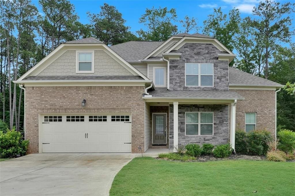 craftsman-style house featuring a garage, stone siding, a front lawn, and concrete driveway