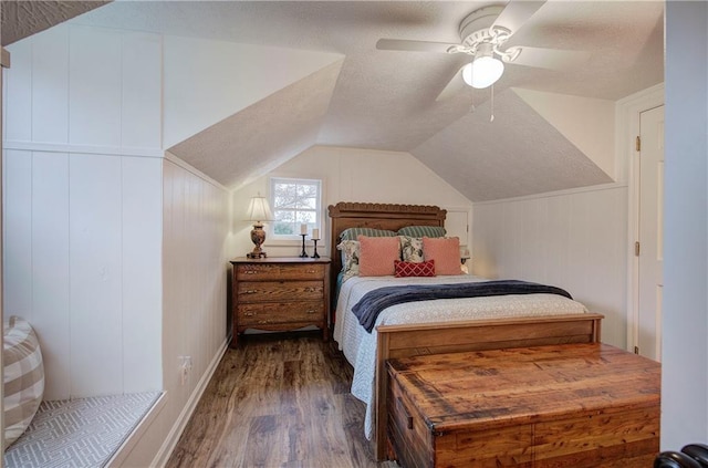 bedroom featuring ceiling fan, wood walls, hardwood / wood-style floors, a textured ceiling, and lofted ceiling