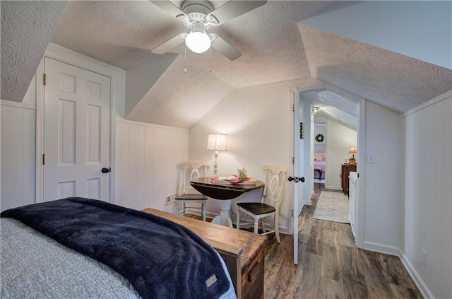 bedroom with a textured ceiling, ceiling fan, wood-type flooring, lofted ceiling, and wood walls