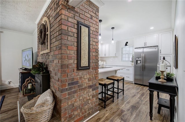 kitchen with stainless steel refrigerator with ice dispenser, decorative light fixtures, hardwood / wood-style flooring, white cabinets, and ornamental molding