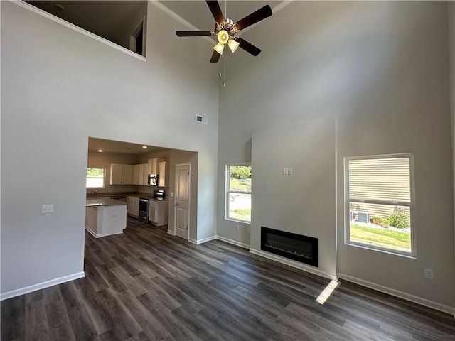 unfurnished living room featuring dark hardwood / wood-style flooring, high vaulted ceiling, and ceiling fan