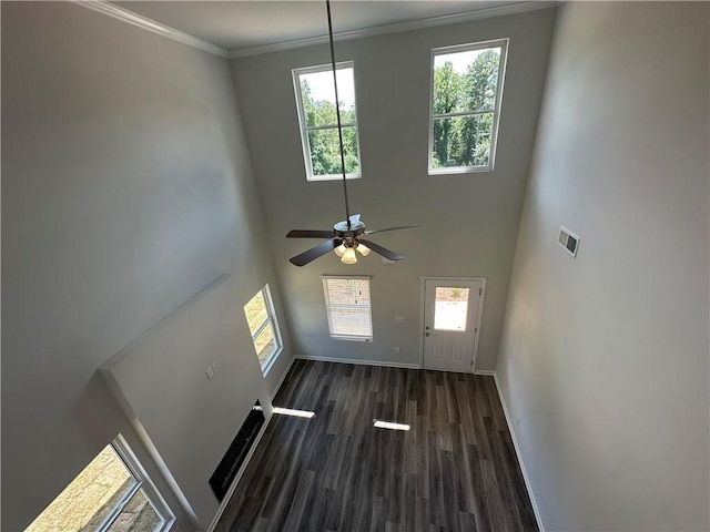 unfurnished living room with ceiling fan, dark hardwood / wood-style flooring, a towering ceiling, and ornamental molding