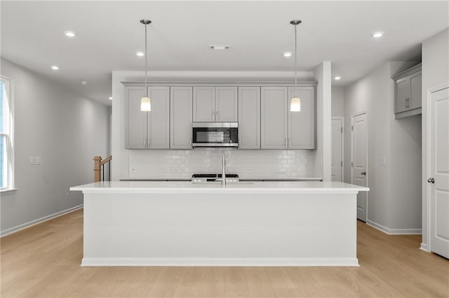 714 Smokey Quartz Way, Kennesaw, GA 30144 - kitchen featuring stainless steel microwave, gray cabinets, decorative backsplash, light countertops, and a kitchen island with sink
