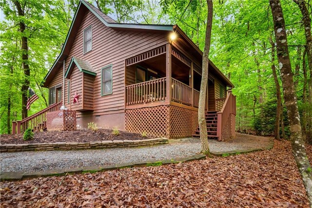 chalet / cabin featuring covered porch, crawl space, a view of trees, gravel driveway, and a sunroom