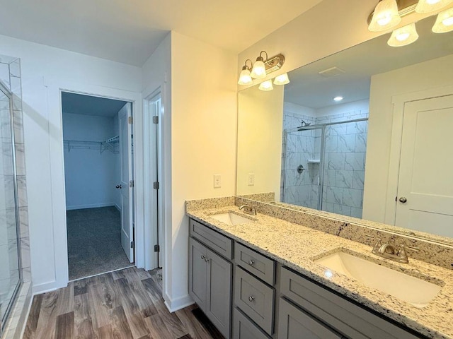 full bathroom featuring a walk in closet, a shower stall, wood finished floors, and a sink